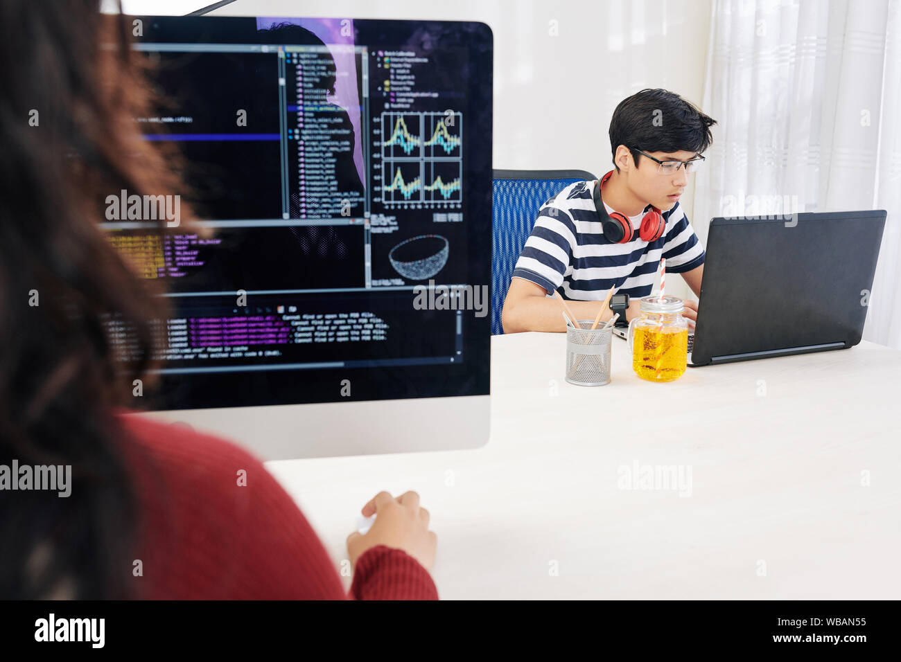 Concentrated Asian teenager programming on laptop in office, his female ...