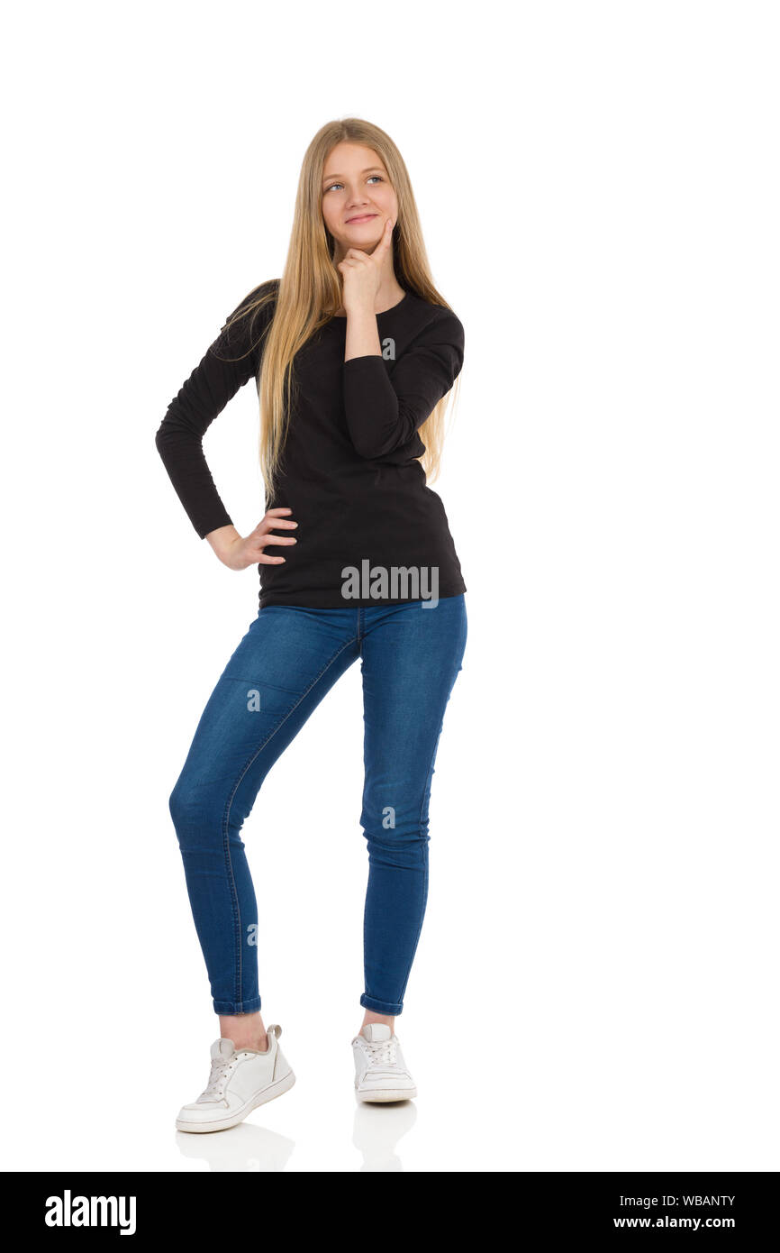 Teenage girl in jeans, sneakers and black blouse is standing, holding hand  on chin, looking away and smiling. Front view. Full length studio shot isol  Stock Photo - Alamy