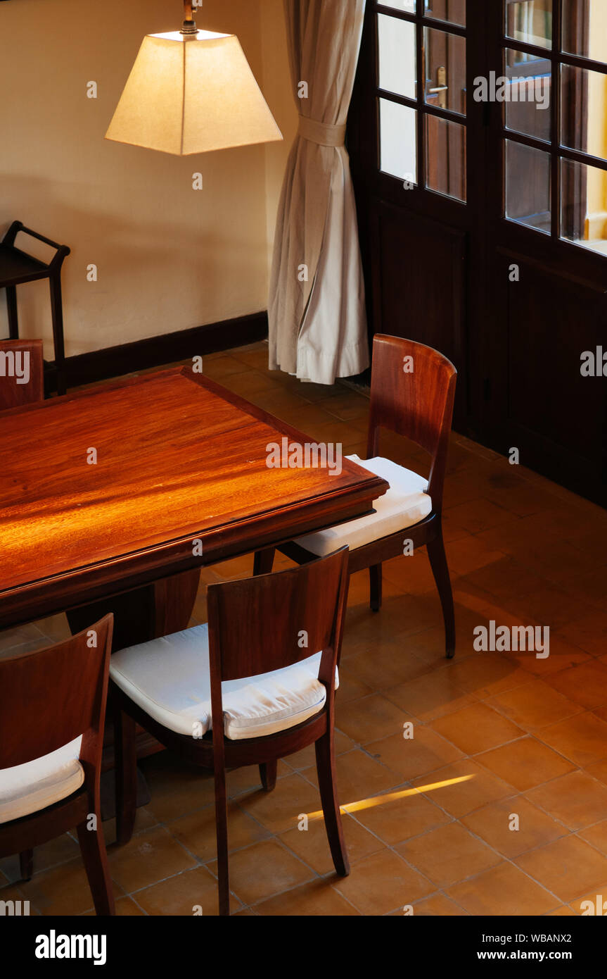 FEB 25, 2014 Dalat, Vietnam - Vintage colonial ceramic tile floor dinner room with hard wood table, chair, white curtain and classic pedant lamp. Stock Photo