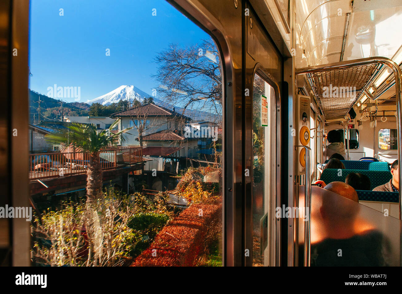 NOV 30, 2018 Fujiyoshida, Japan - Snow covered Mount Fuji behind local town along train route from Tokyo to Kawaguchiko seen through train window with Stock Photo