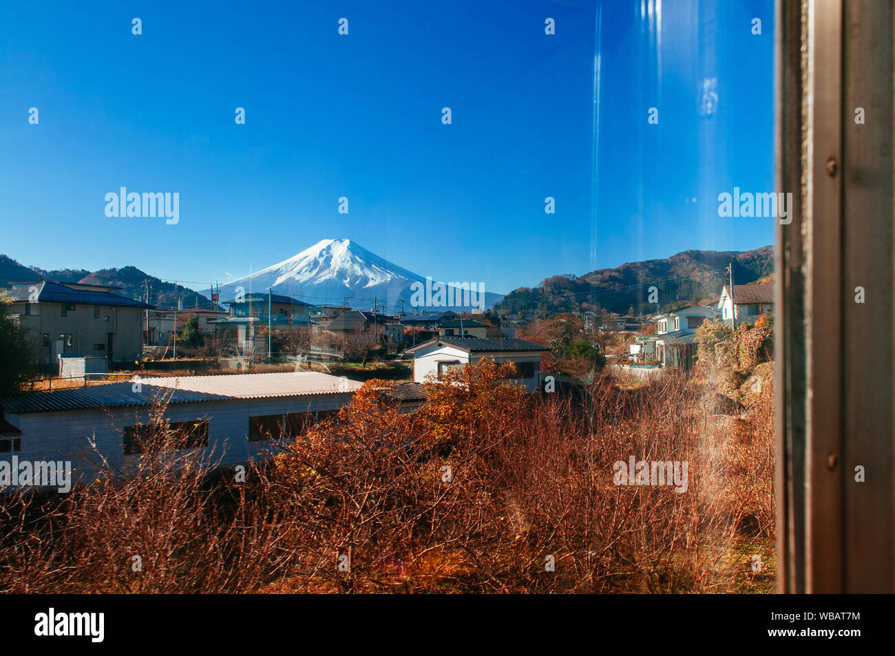 Snow covered Mount Fuji and local town along train route from Tokyo to Kawaguchiko seen through train window with some mirror reflect on right side Stock Photo