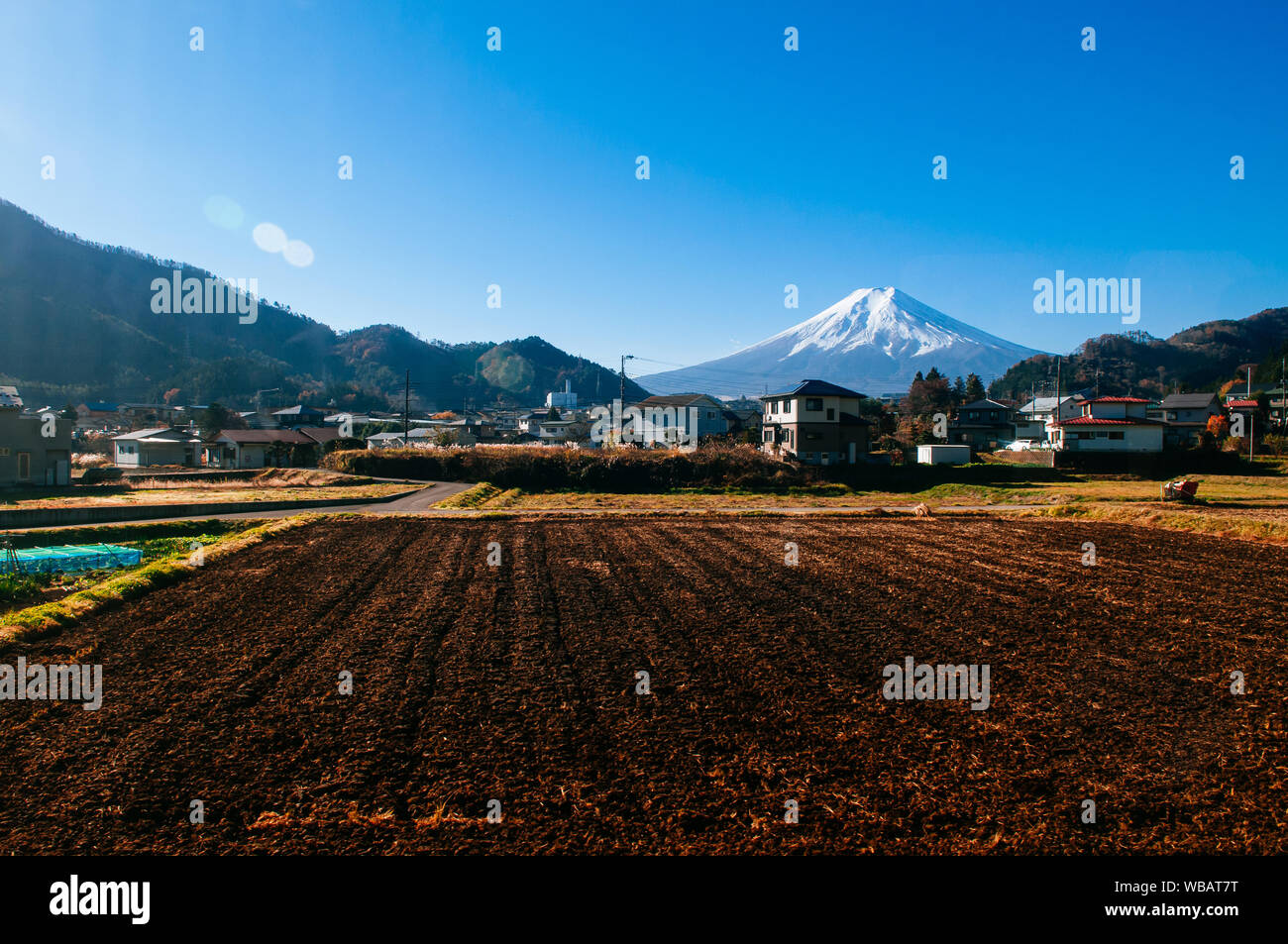 Snow covered Mount Fuji and local town along train route from Tokyo to Kawaguchiko seen through train window with some mirror reflect on left side Stock Photo