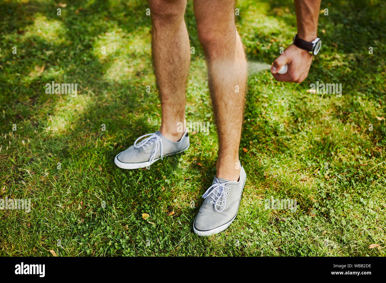 Man using spray bottle of insect repellent on his leg outdoors Stock Photo