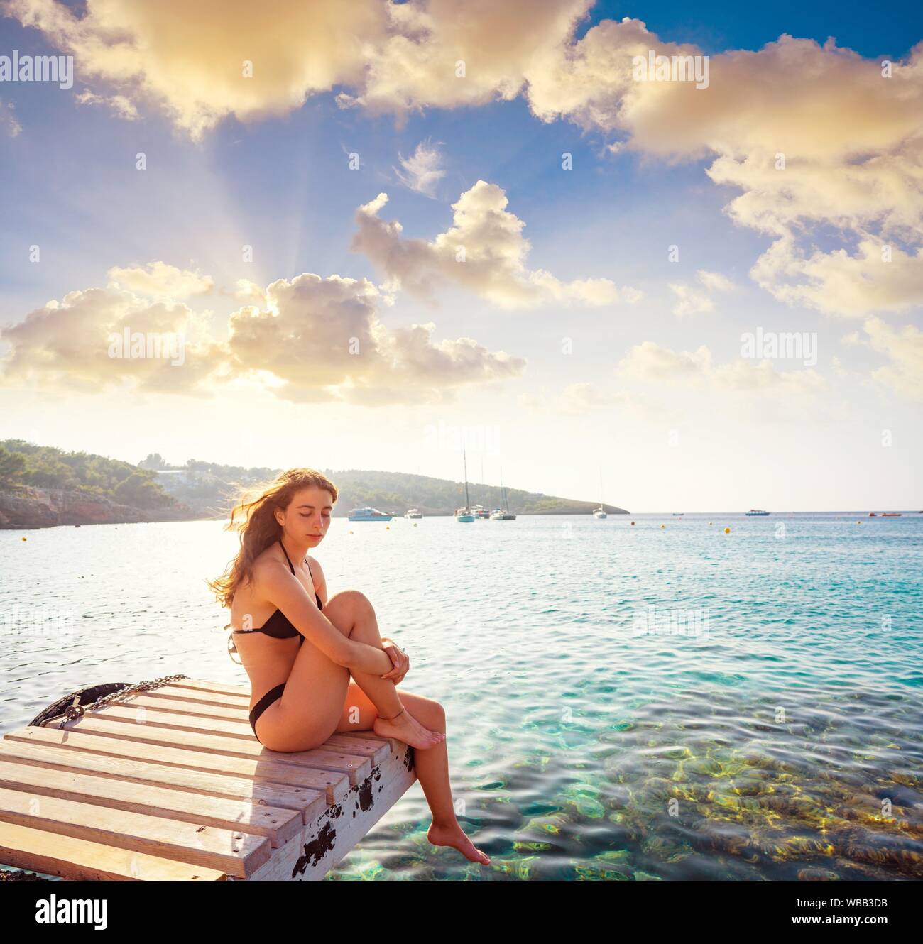 Ibiza bikini girl relaxed at Portinatx beach pier sunset in Balearic Islands. Stock Photo