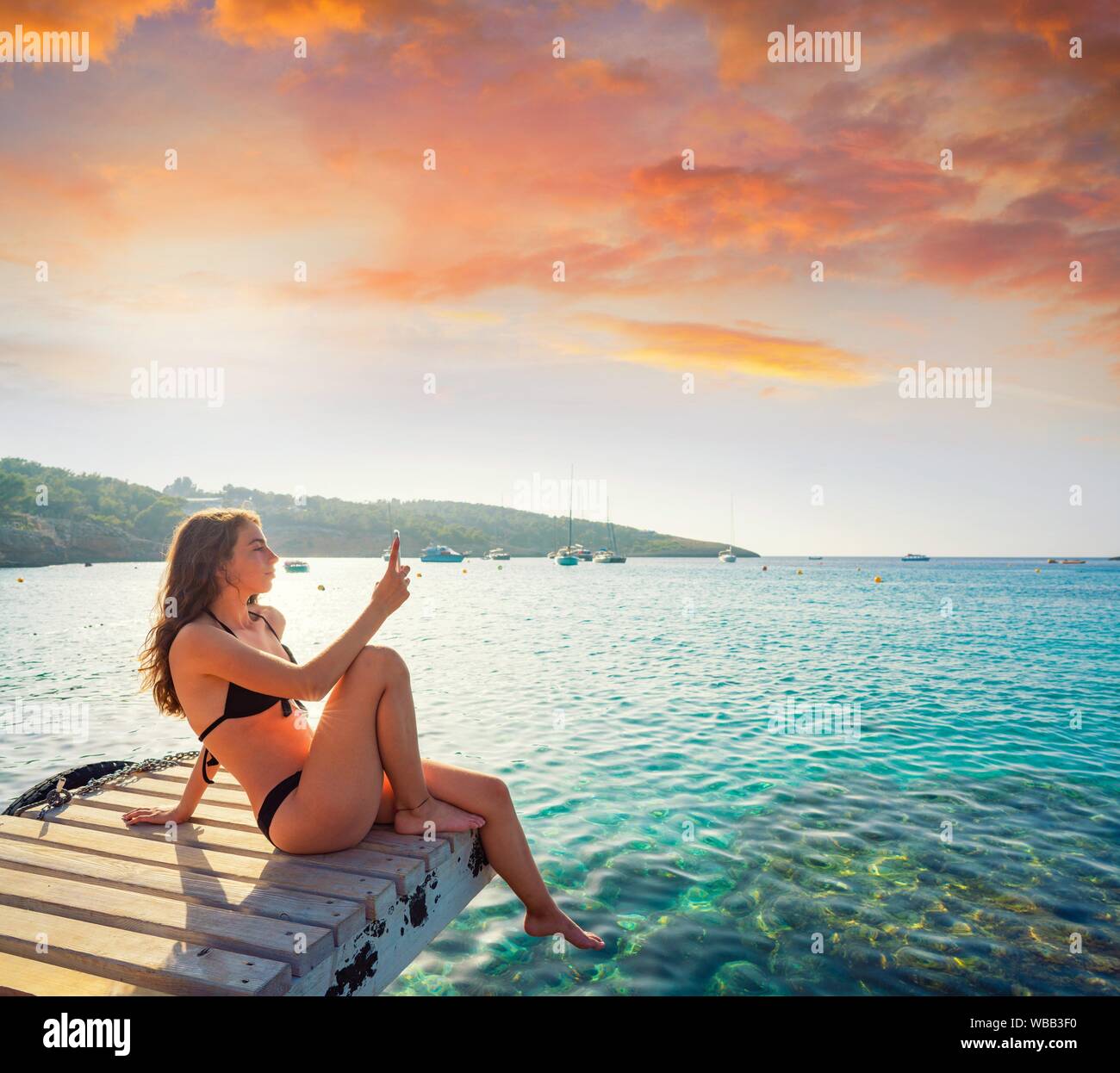 Ibiza girl taking smartphone photos at Portinatx beach pier in Balearic Islands. Stock Photo