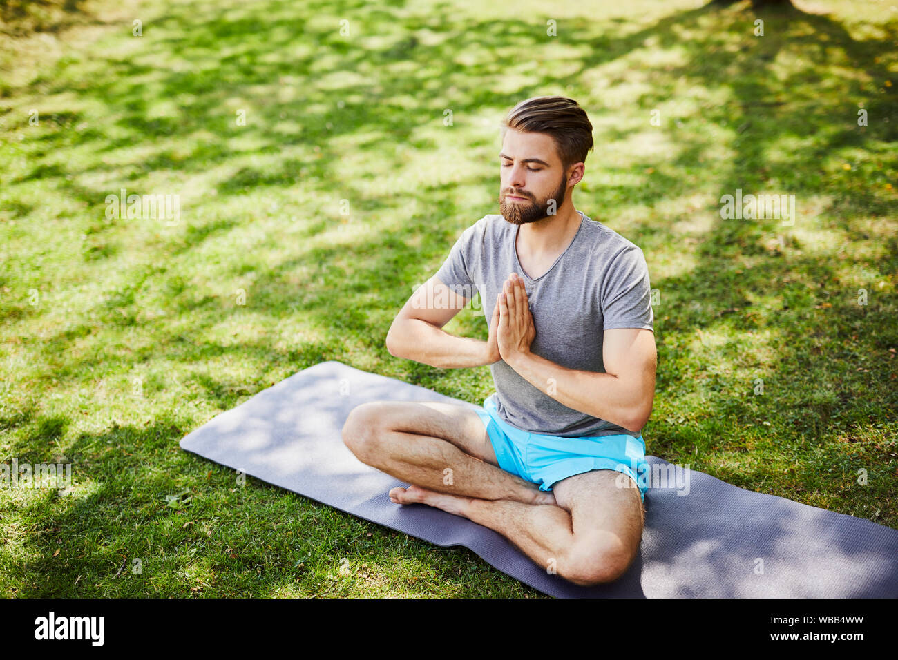 Young man meditating outdoors in the park, sitting with eyes closed and ...