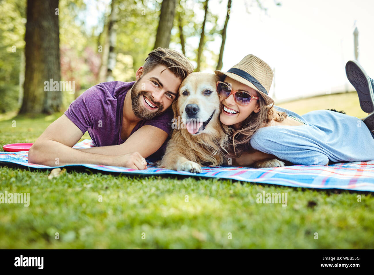 Young couple having picnic with their dog in the park, lying on blanket ...