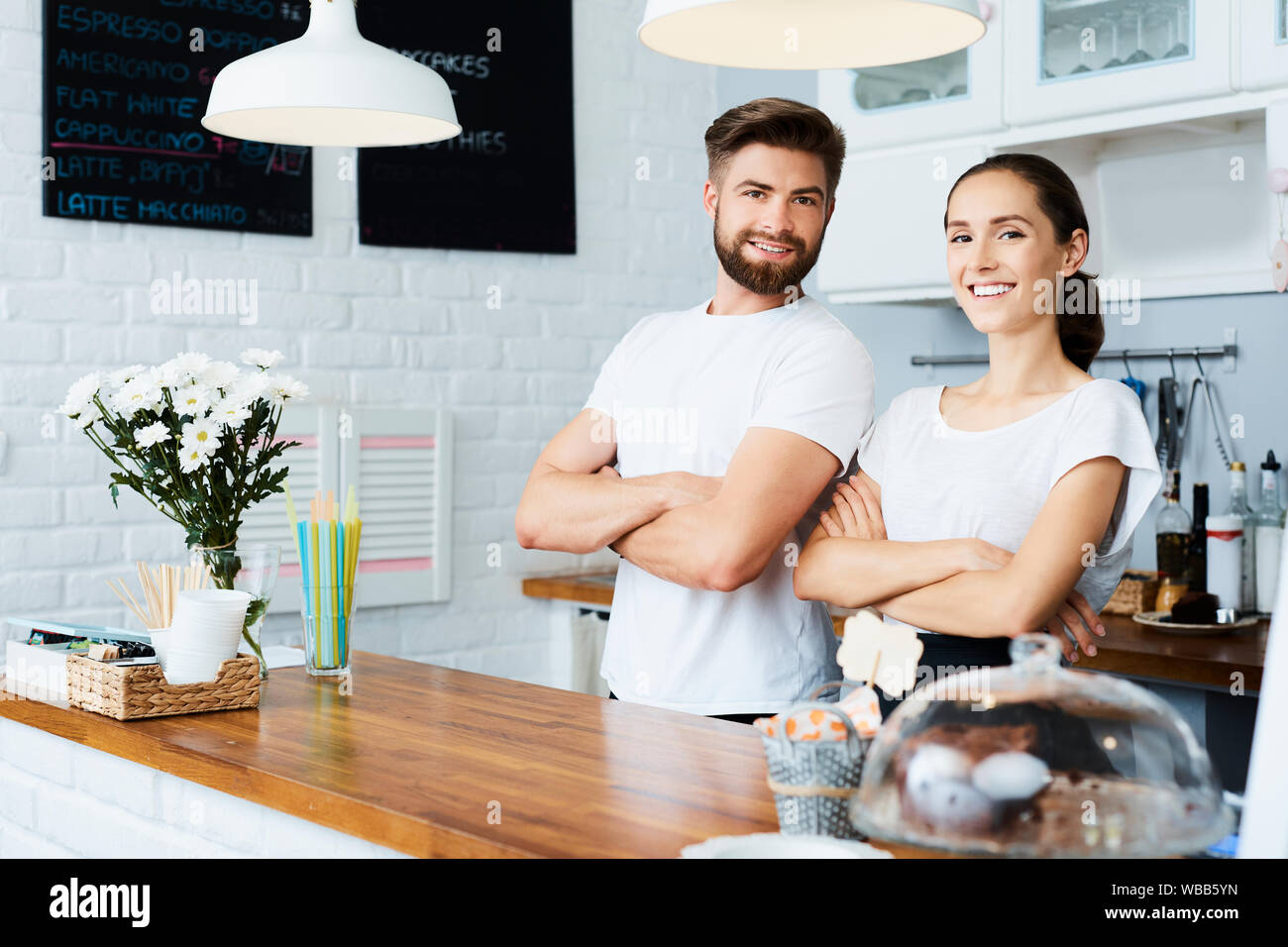 Two cheerful small business owners smiling and looking at camera while standing behind the counter in their restaurant Stock Photo
