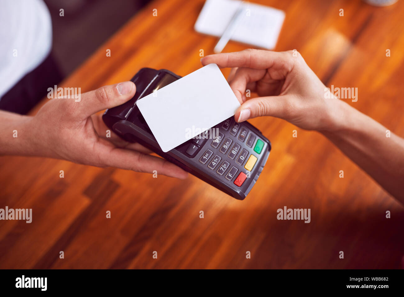 Closeup shot of female hand paying with card with wooden counter in background Stock Photo