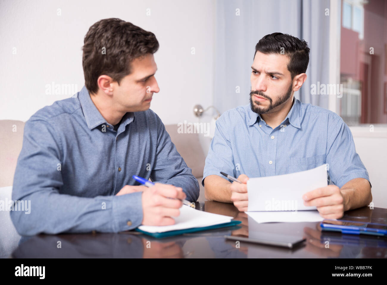 Two young men in serious discussion at home table while analysing documents together Stock Photo