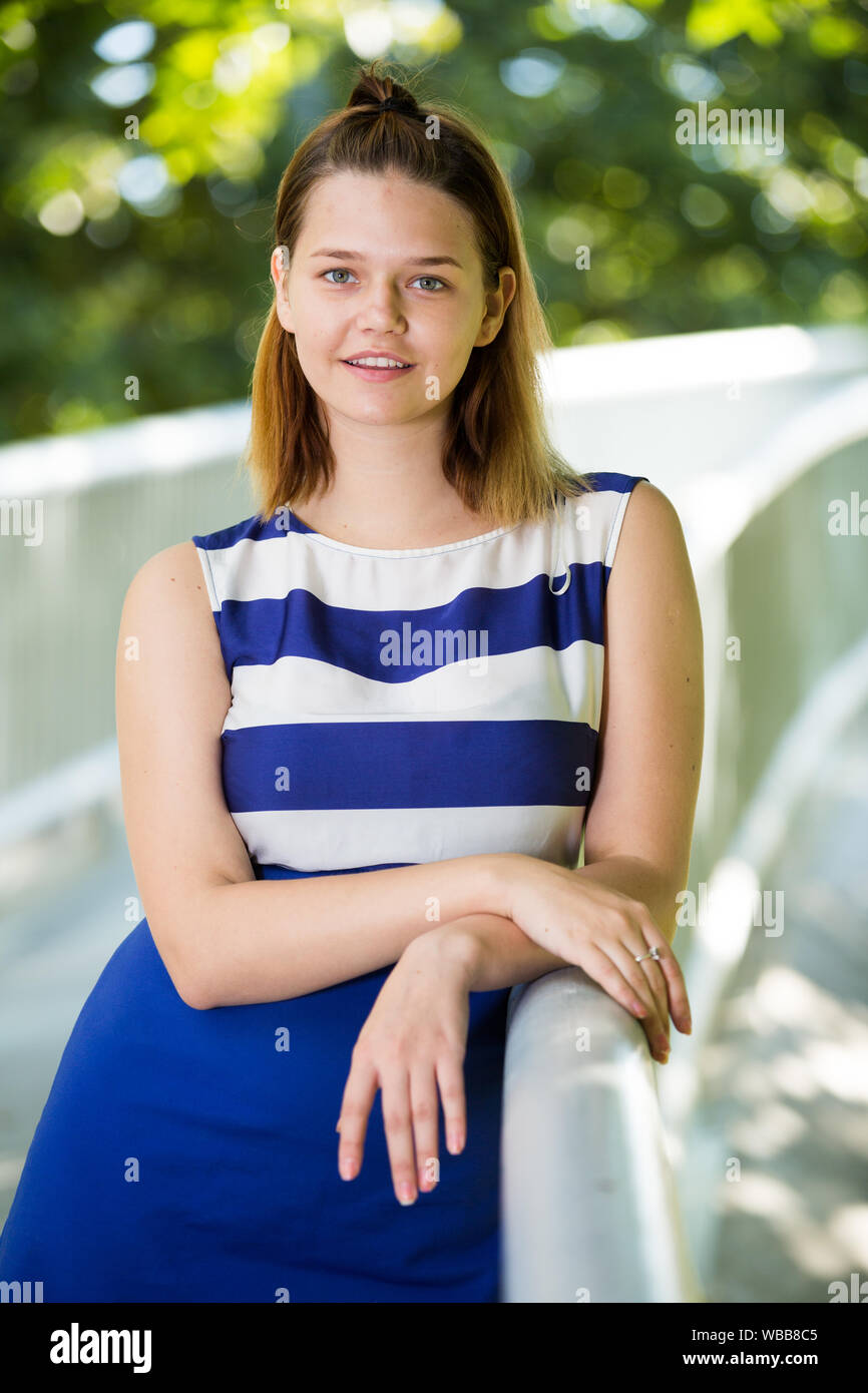 Portrait of young stylish girl standing on bridge in summer city park ...