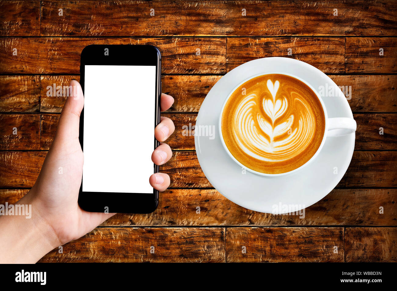 hand holding phone with coffee latte on top view wood textured background Stock Photo