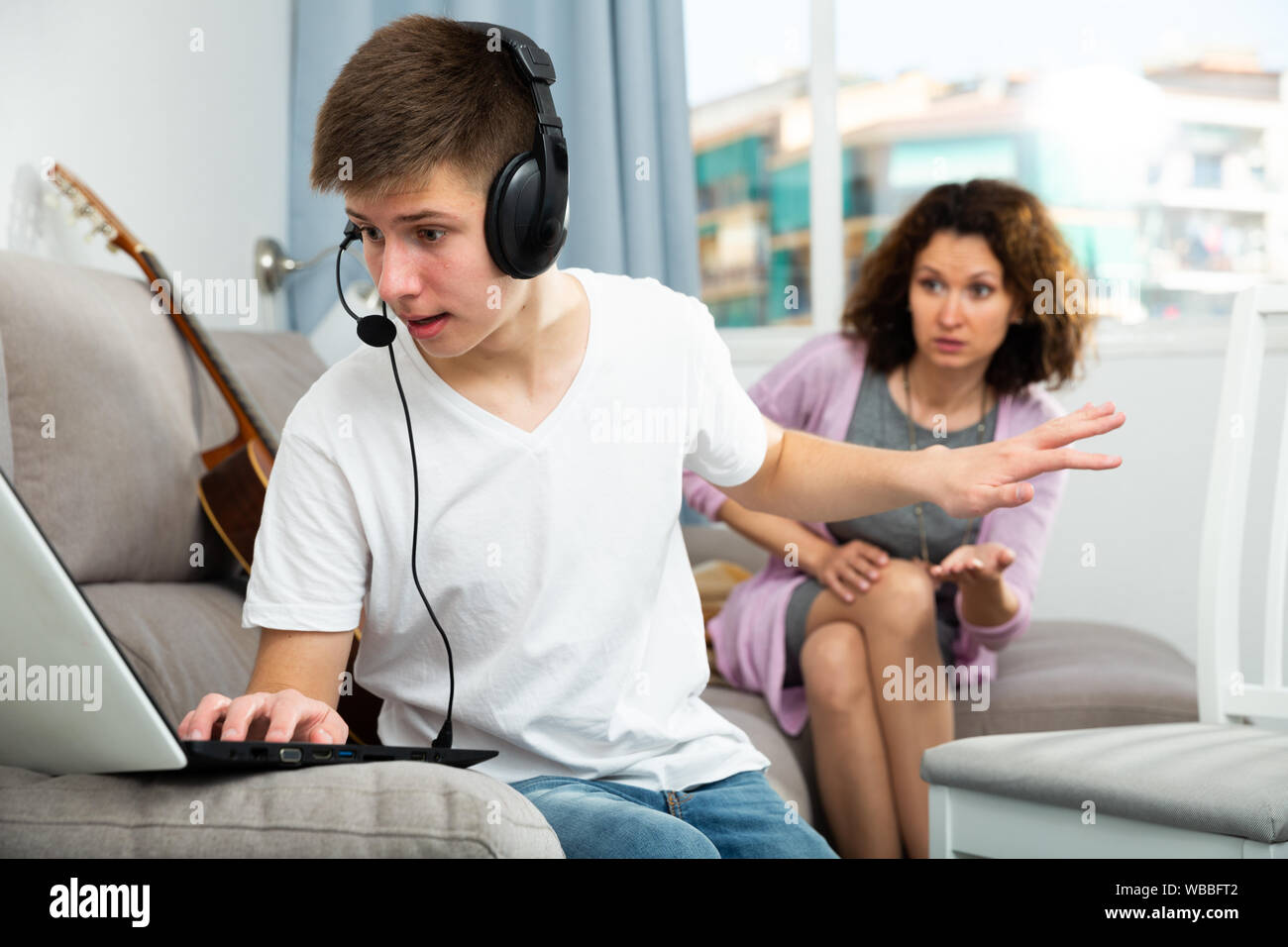 Teenage son listening music in headphones or playing online games ignoring  his mother Stock Photo - Alamy