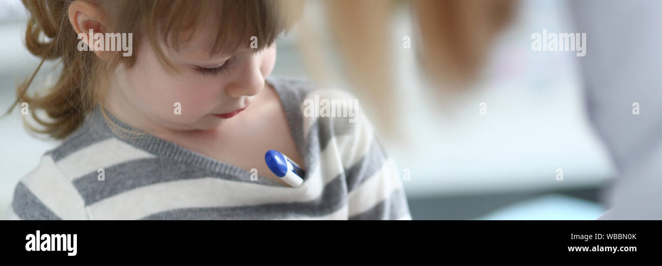 Cute pensive little girl with thermometer under her armpit Stock Photo