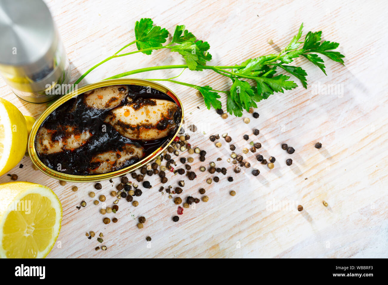 Canned seafood. Stuffed little squids (chipirones) in ink served in open tin can with herbs and lemon on wooden table Stock Photo