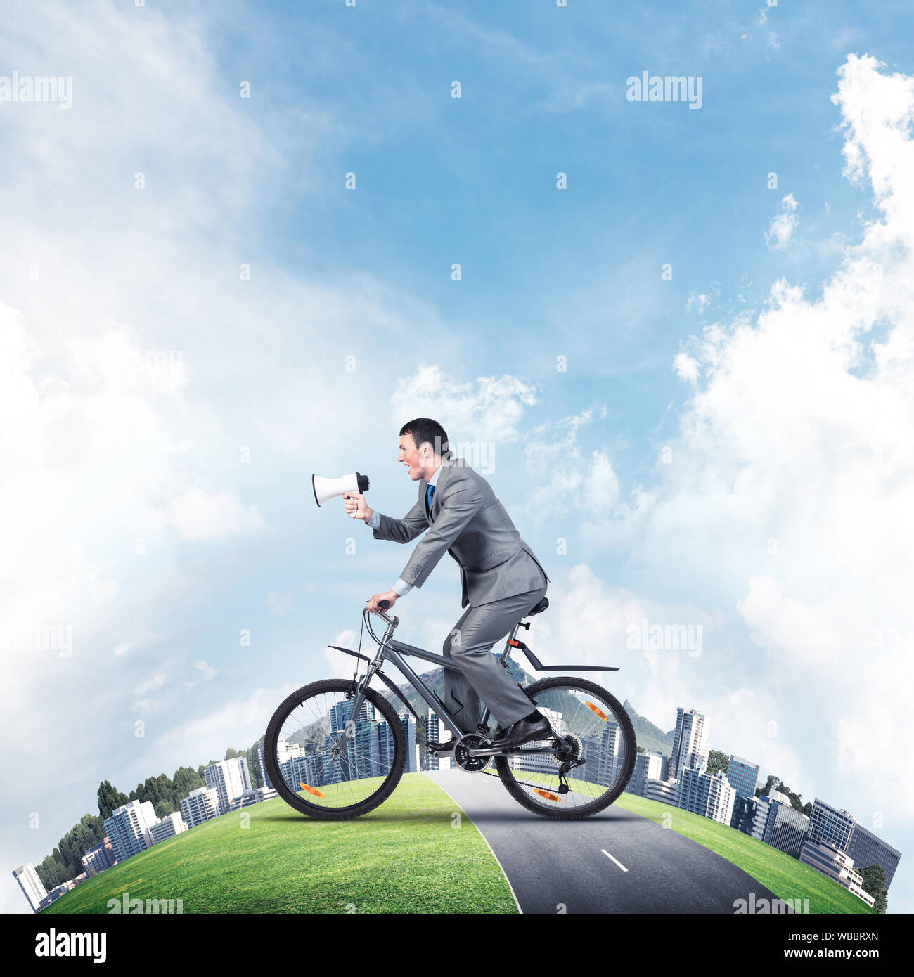 Businessman with megaphone in hand on bike. Corporate employee announcing in loudspeaker. Man in business suit riding bicycle on road. Handsome cyclis Stock Photo