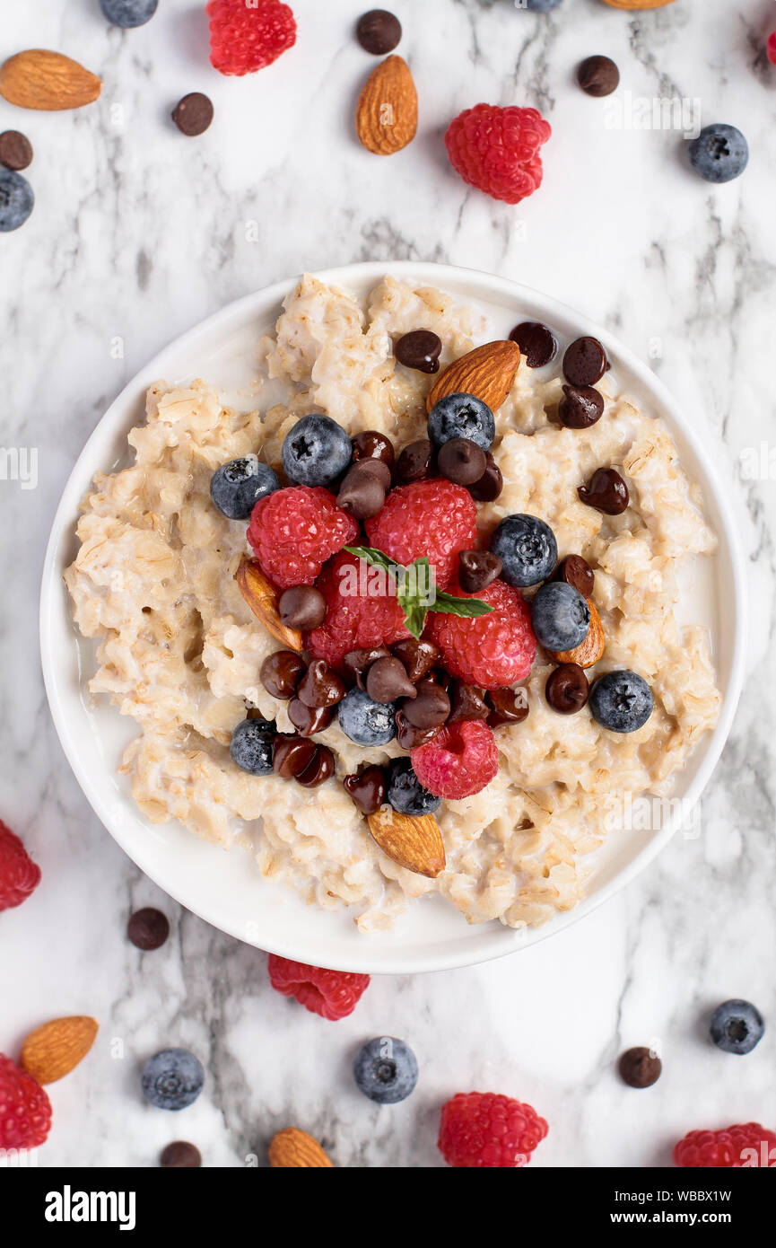 Healthy oatmeal served with berries, chocolate chips, almonds and honey over a marble table background. Shot from top view. Stock Photo