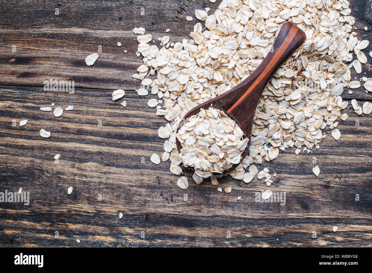 Healthy raw uncooked quick oat flakes in a wooden spoon over a wood table background. Shot from top view. Stock Photo