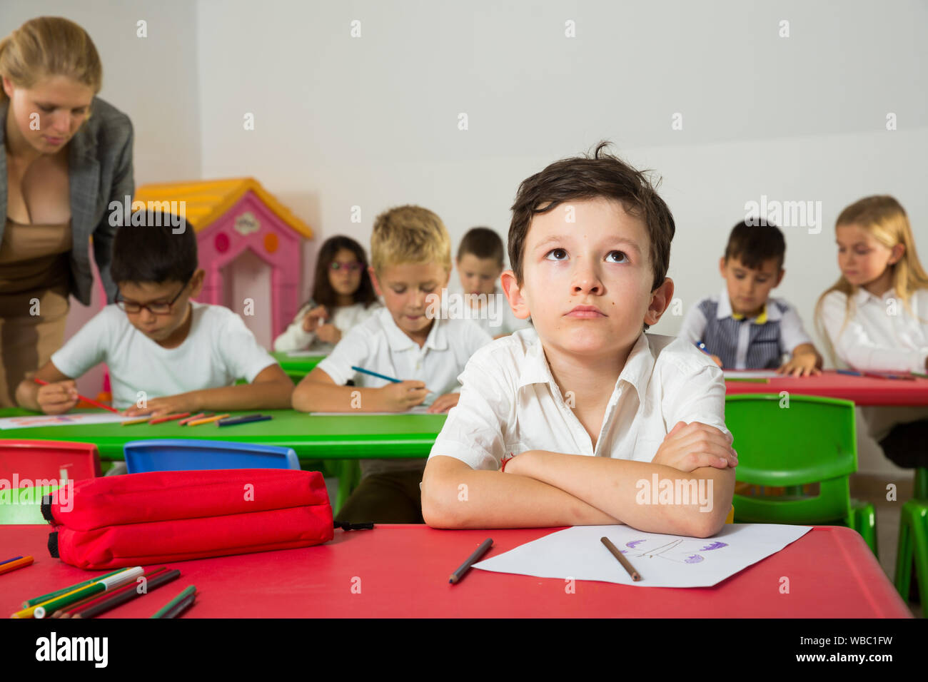 Portrait of bored schoolboy sitting in classroom with classmates and ...