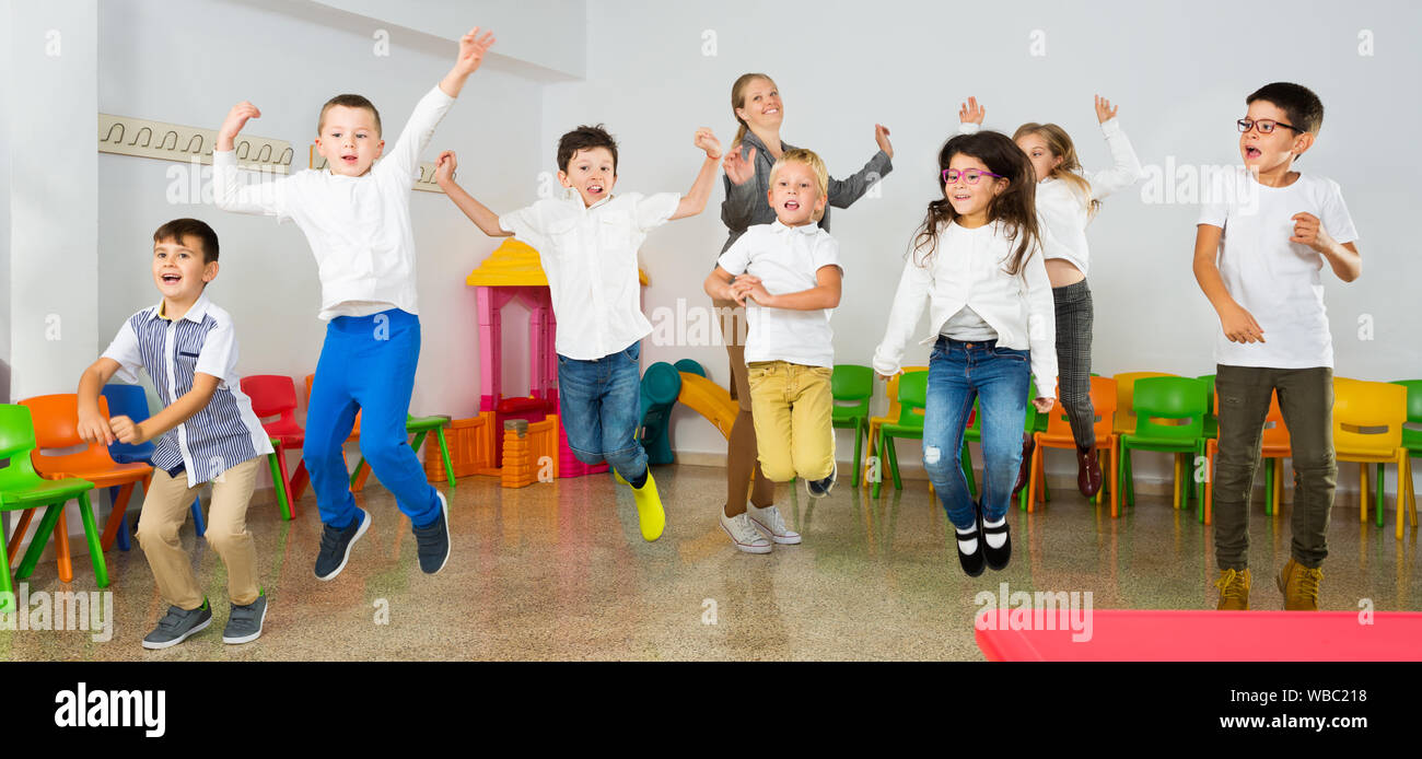 Group of happy cheerful children with their female teacher jumping ...