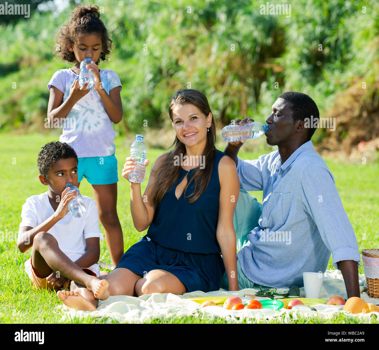 Happy mixed race family with two children enjoying picnic on green