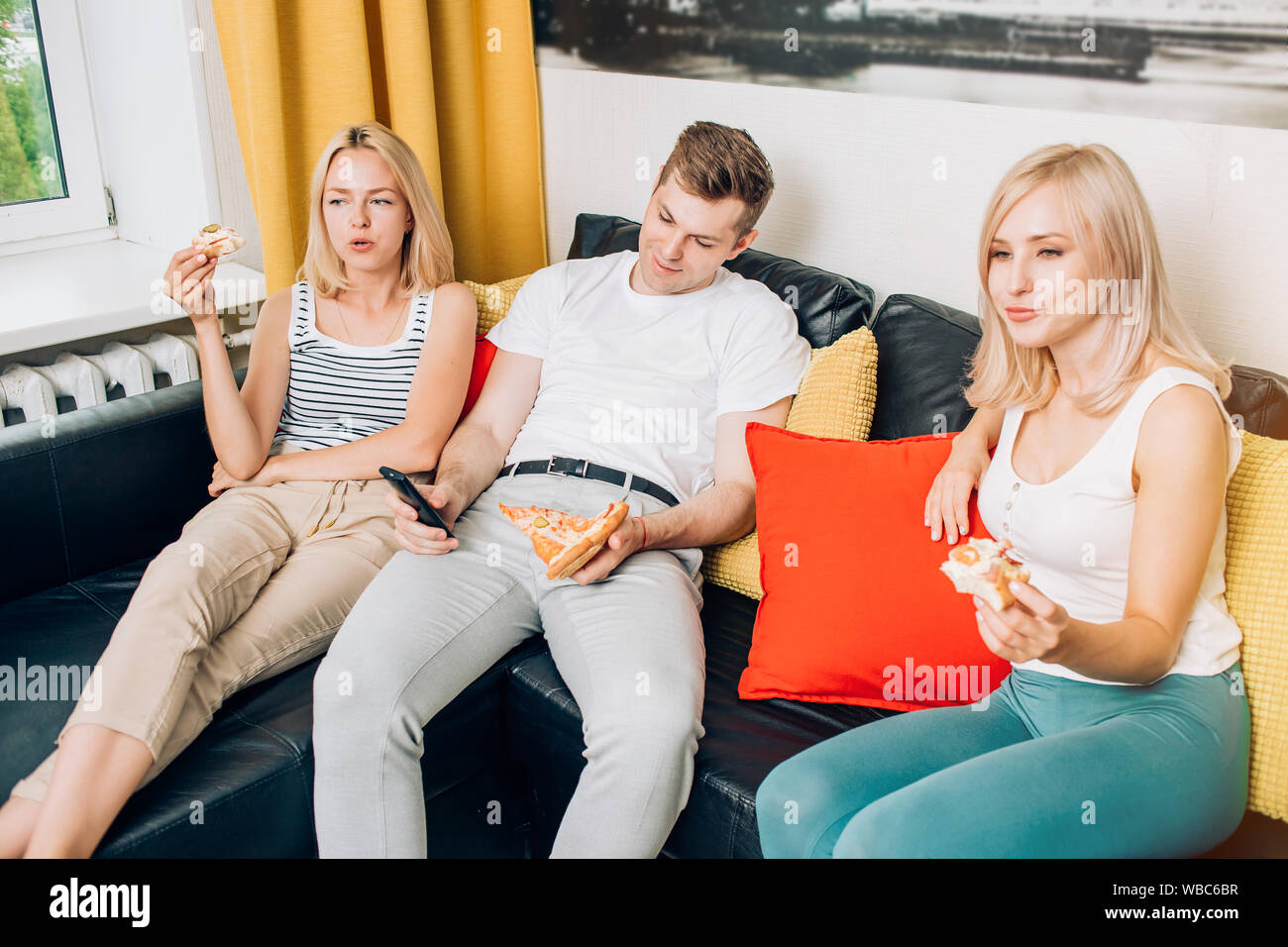 Young People In Casual Clothes Eating Pizza Sitting On Sofa
