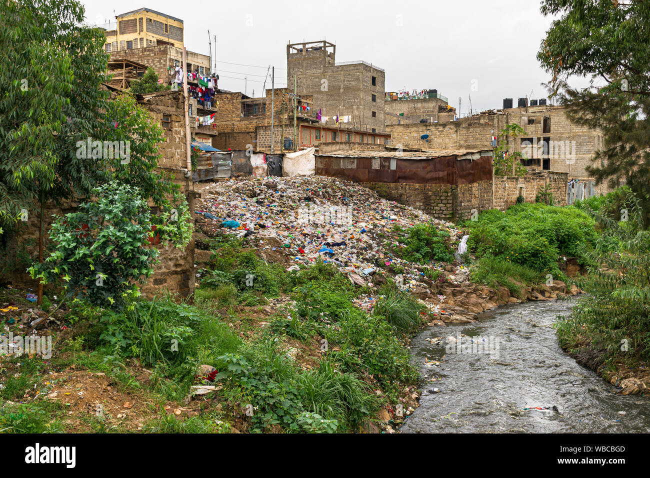 Mathare river with large pile of rubbish on the ground next to it behind housing, Nairobi, Kenya Stock Photo