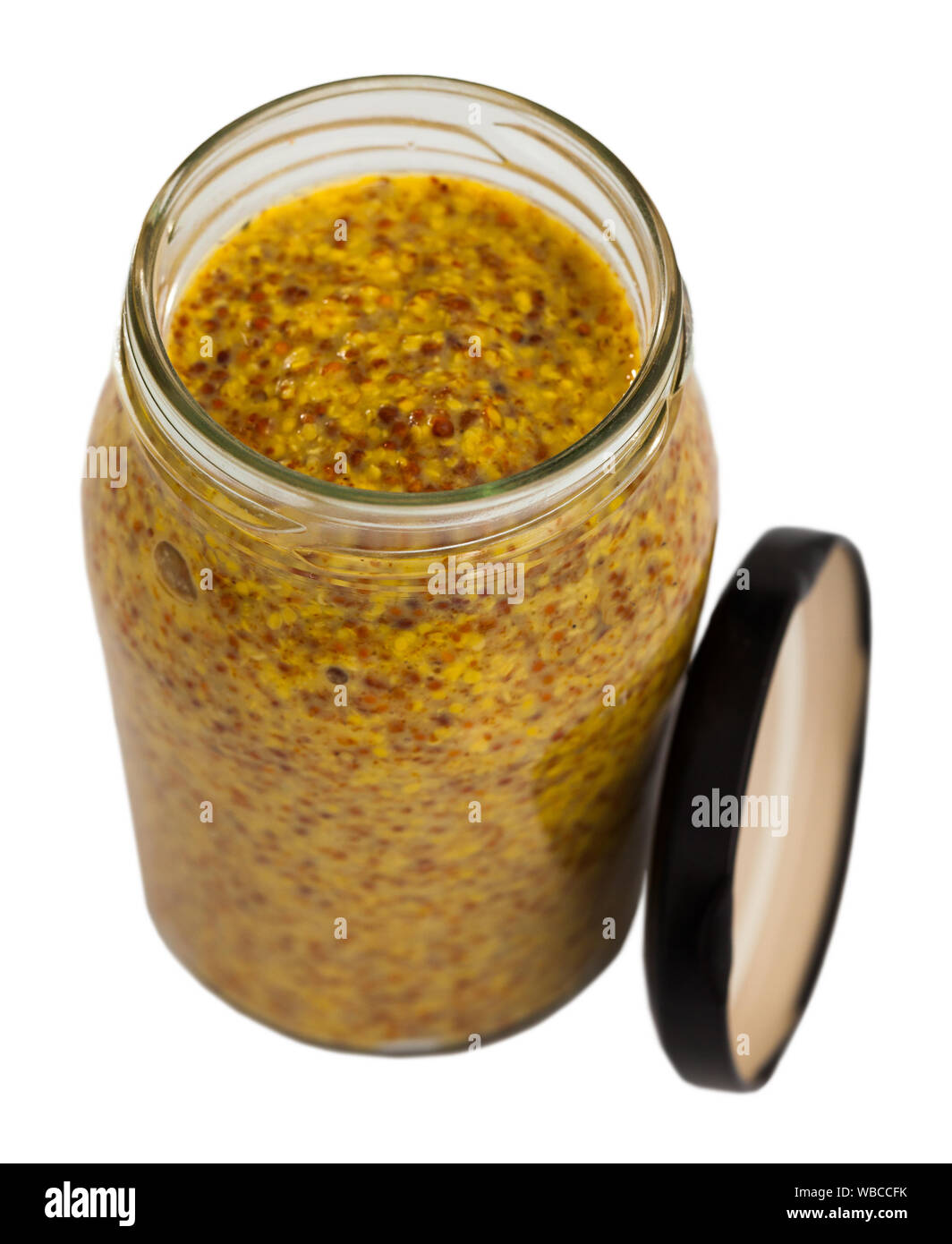 Soft and mild grainy mustard in open glass jar. Isolated over white