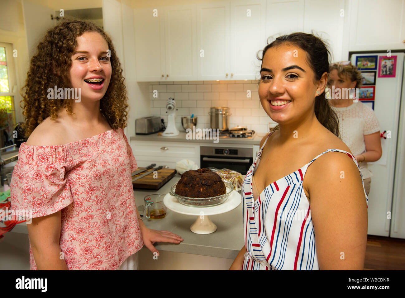 Two young teenage Australian girls smiling and preparing to light a Christmas pudding at a Christmas lunch in a modern Sydney kitchen Stock Photo