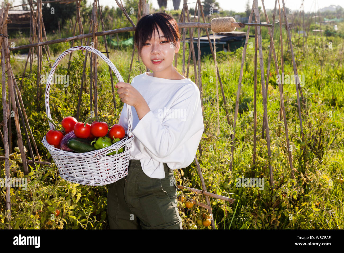 Portrait of young Asian woman holding basket full of harvested ...