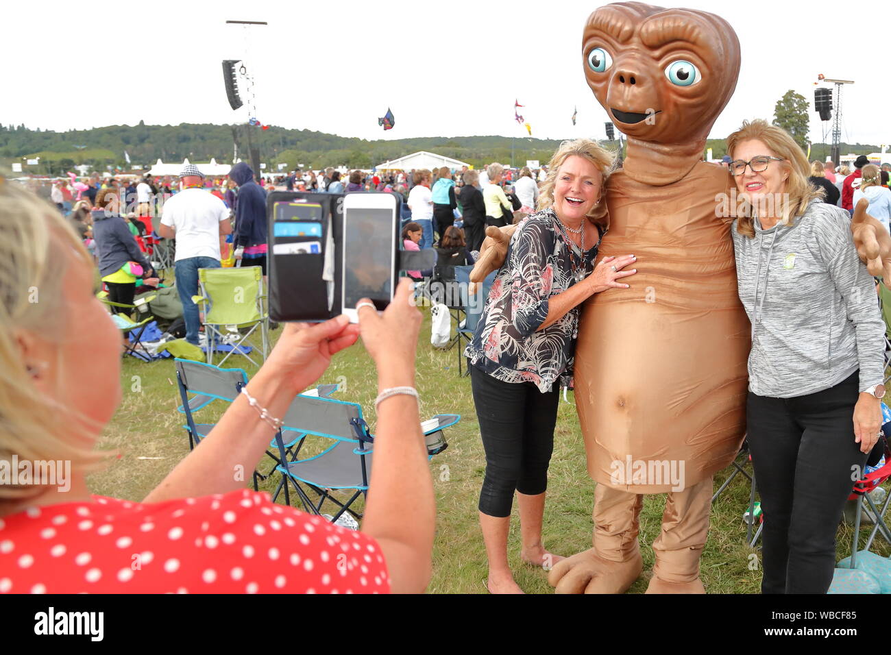A woman taking pictures of friends with a character of ET at the  80's music at the Rewind South music festival at Henley-on-Thames, UK Stock Photo