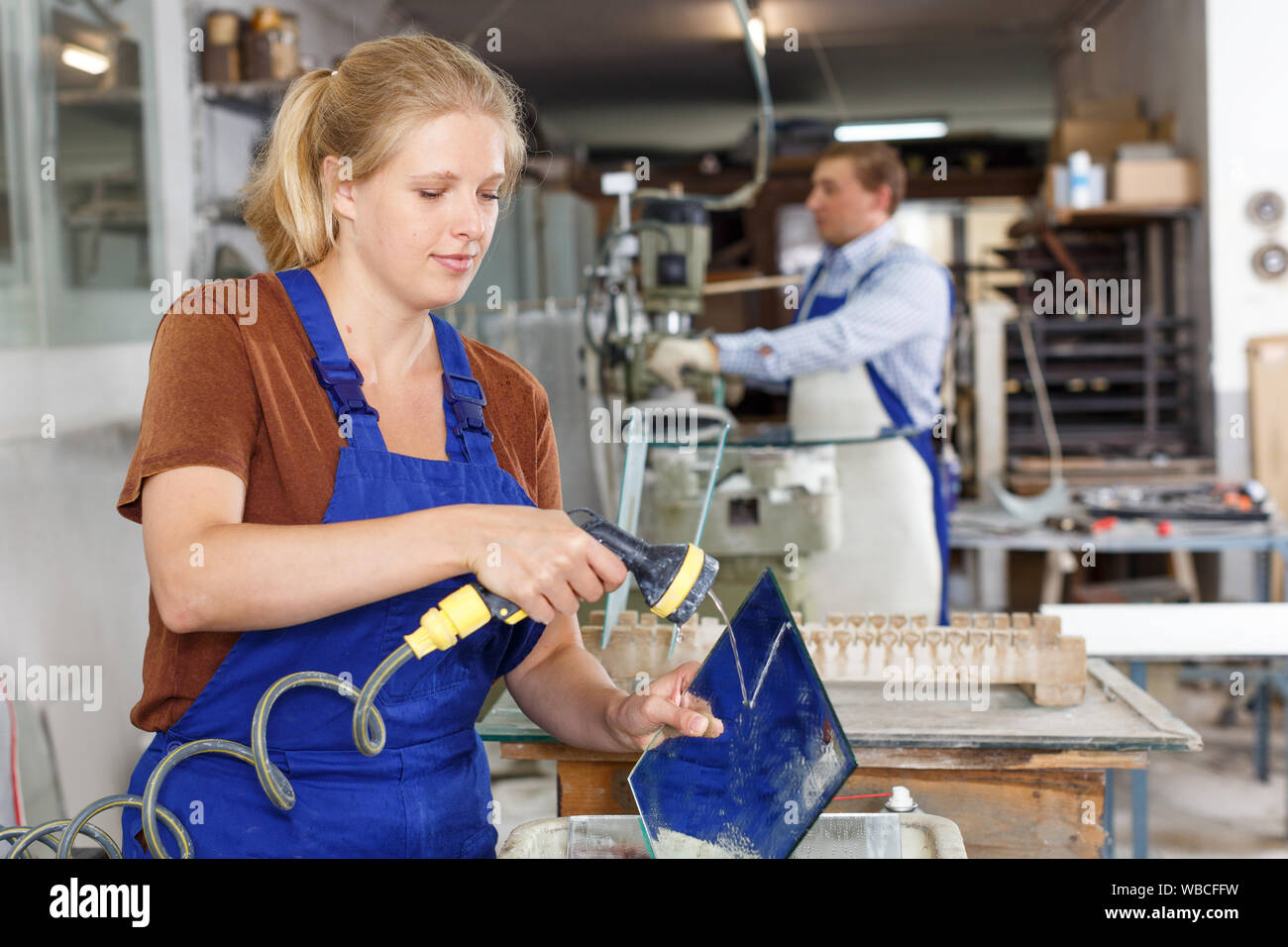 Experienced female worker cleaning cut glass in industrial