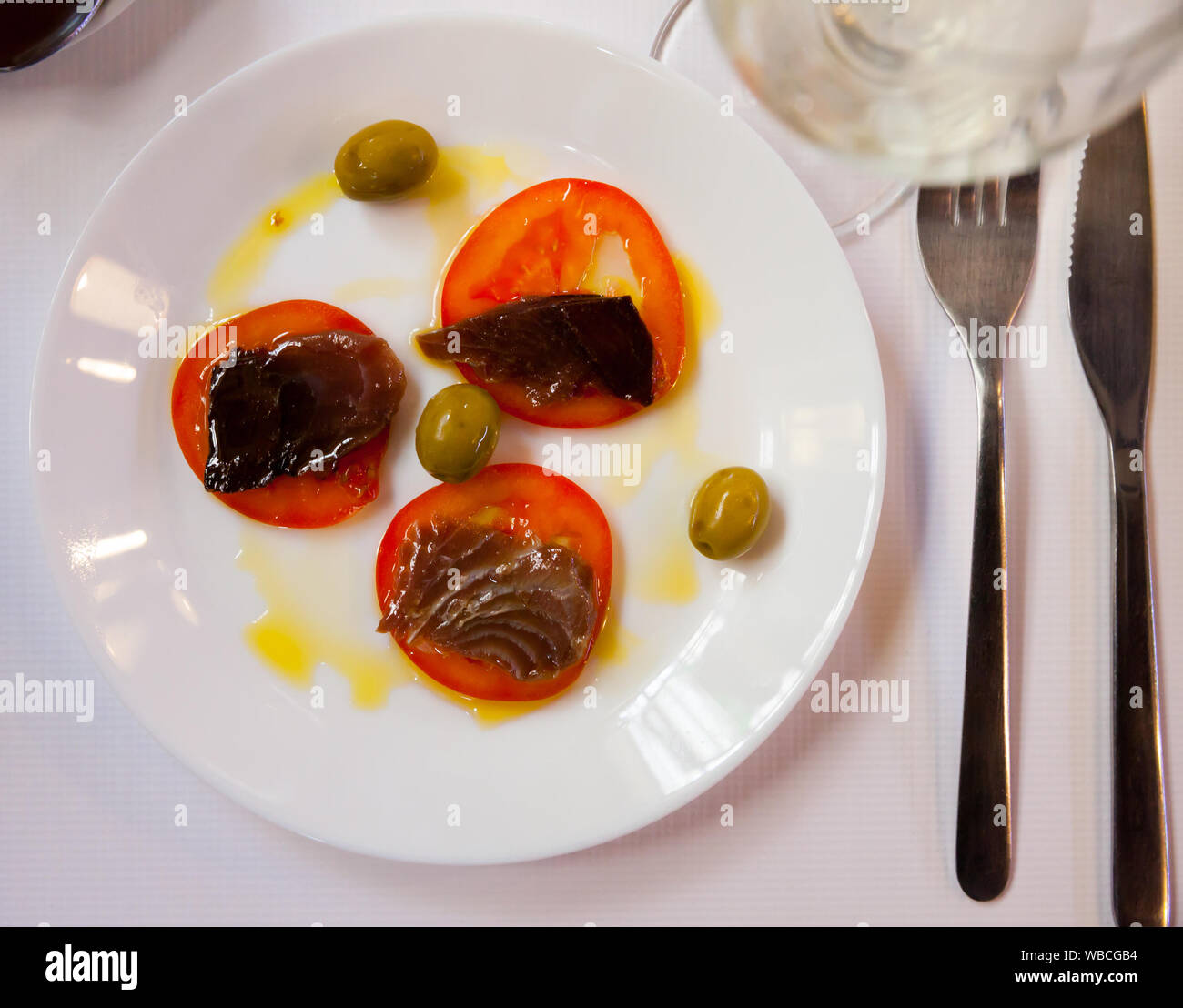 Top view of delicious andalusian tapa of fresh sliced sarda served with tomato, sauce and green olives on white plate Stock Photo