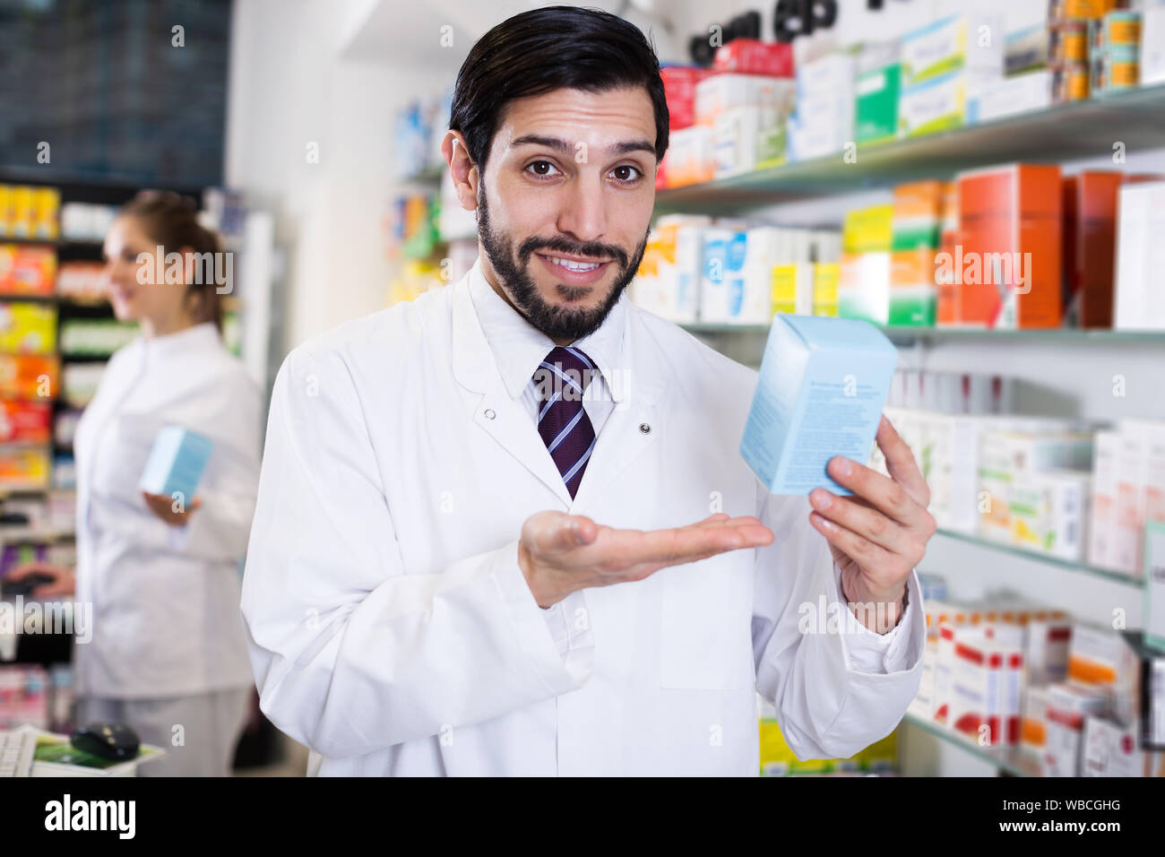 happy adult pharmacist who is standing with medicine on his work place