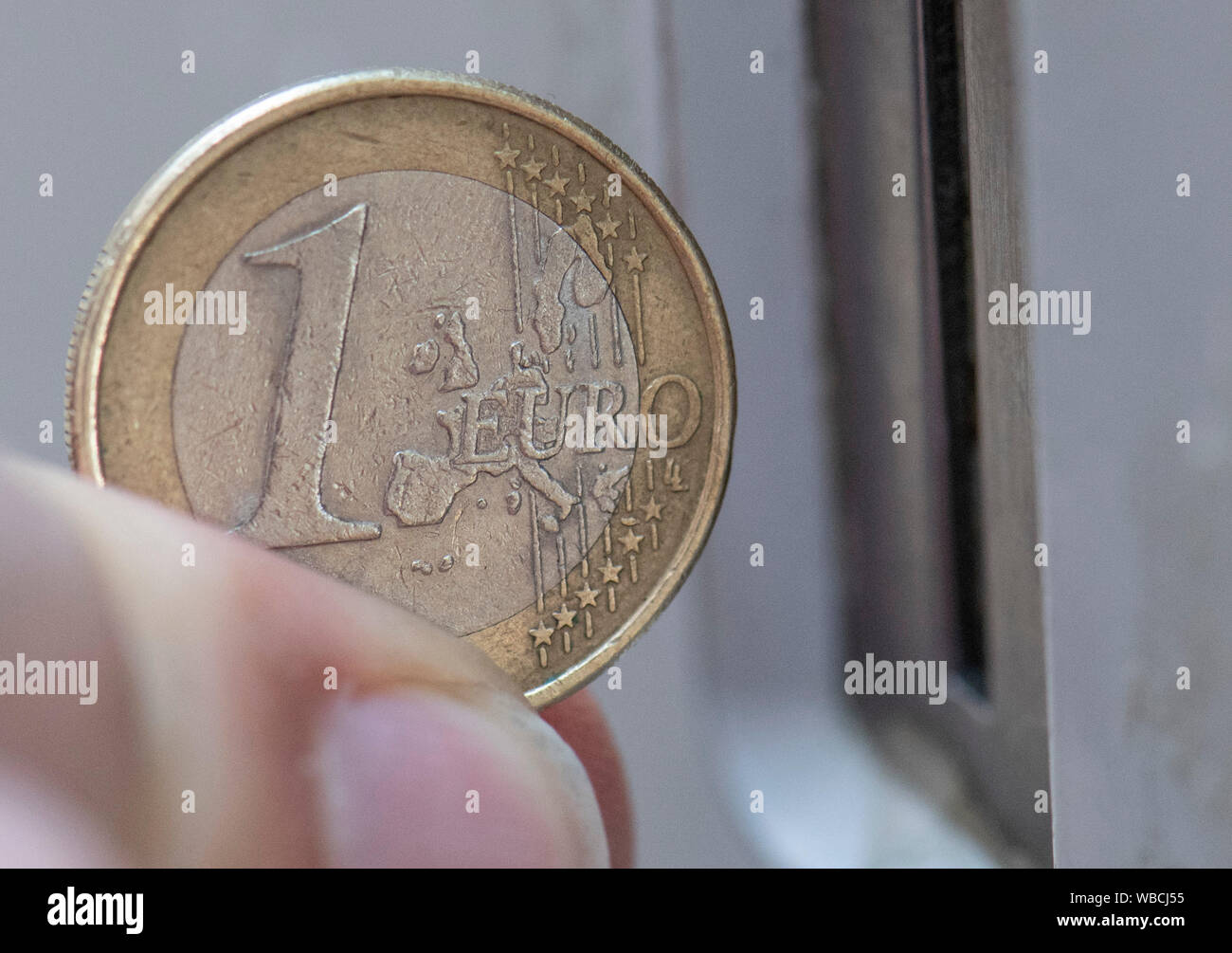 ILLUSTRATION - 26 August 2019, Hessen, Frankfurt/Main: A Euro coin is held in front of the slot of a parking machine. Against the background of an impending ban on diesel driving, parking fees in the city centre are to be raised. Photo: Boris Roessler/dpa Stock Photo