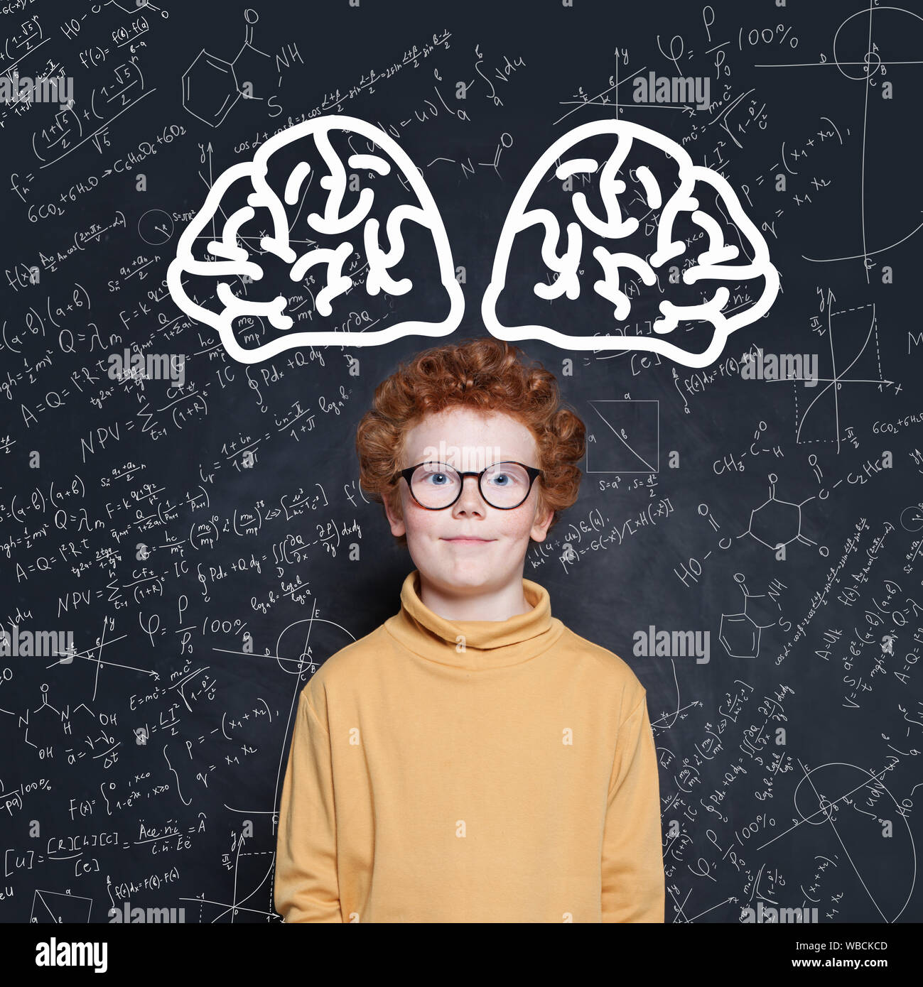 Kid boy with red hair standing against blackboard with science formulas Stock Photo
