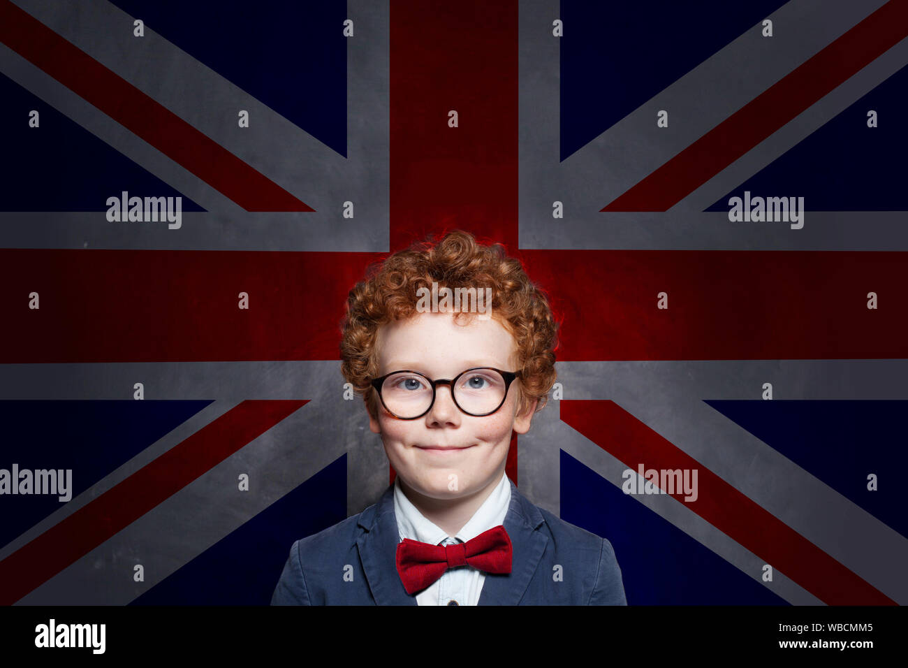 Happy cute kid boy in glasses with the UK flag background. English