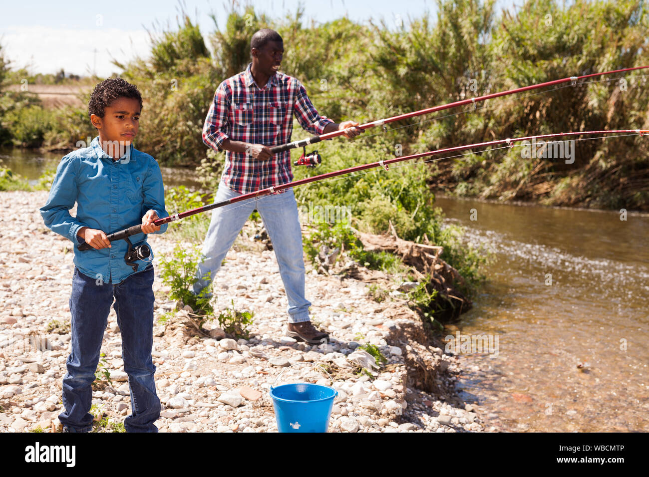 Afro boy holding fishing rod and pulling fish from river Stock Photo