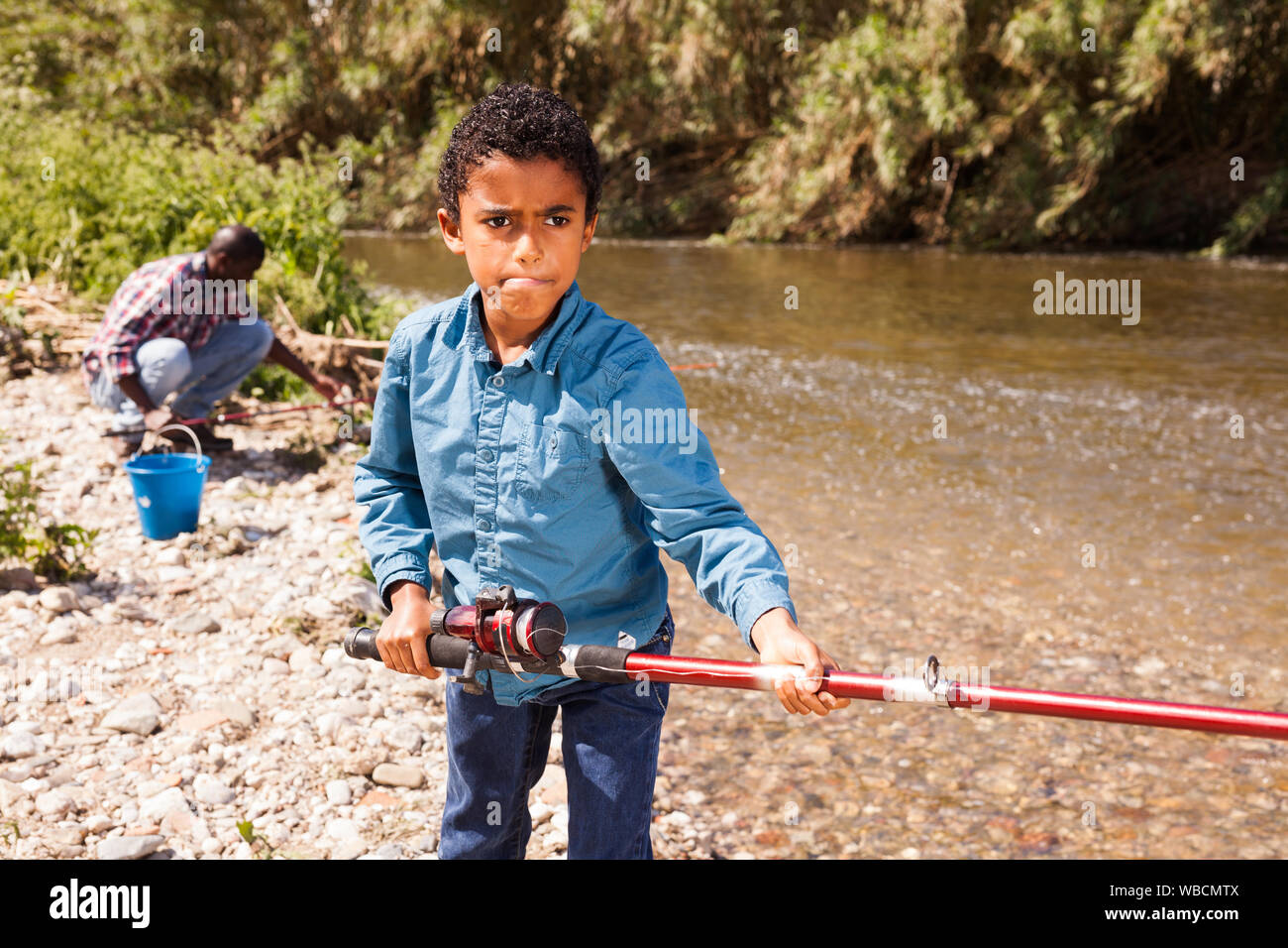 Little African boy fishing with his father and pulling fish Stock Photo