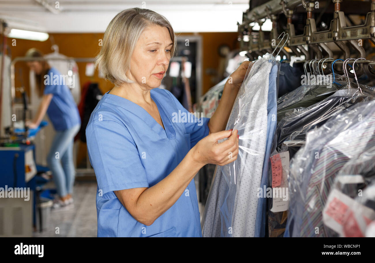 Portrait of female dry-cleaning salon worker on background of coat racks Stock Photo