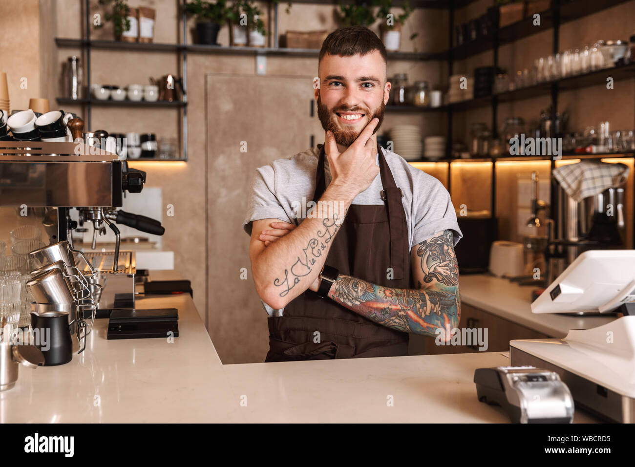 Smiling attractive man barista standing behind the counter at the Smiling attractive man barista standing behind the counter at the