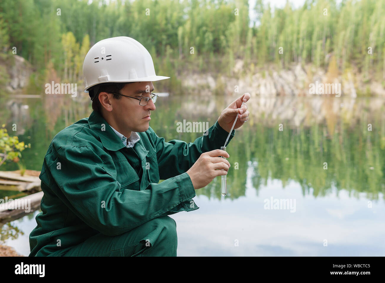 industrial ecologist or chemist takes a sample of water from lake at the site of a flooded mining pit Stock Photo