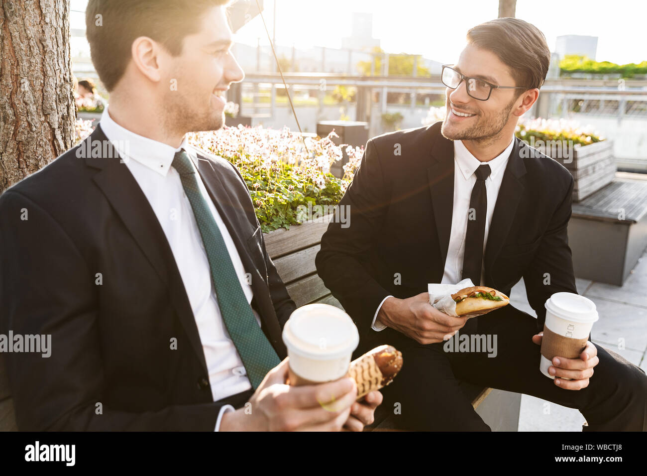 Two attractive smiling young businessmen wearing suits talking while ...