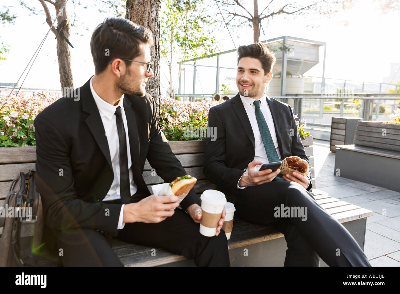 Two attractive smiling young businessmen wearing suits talking while ...