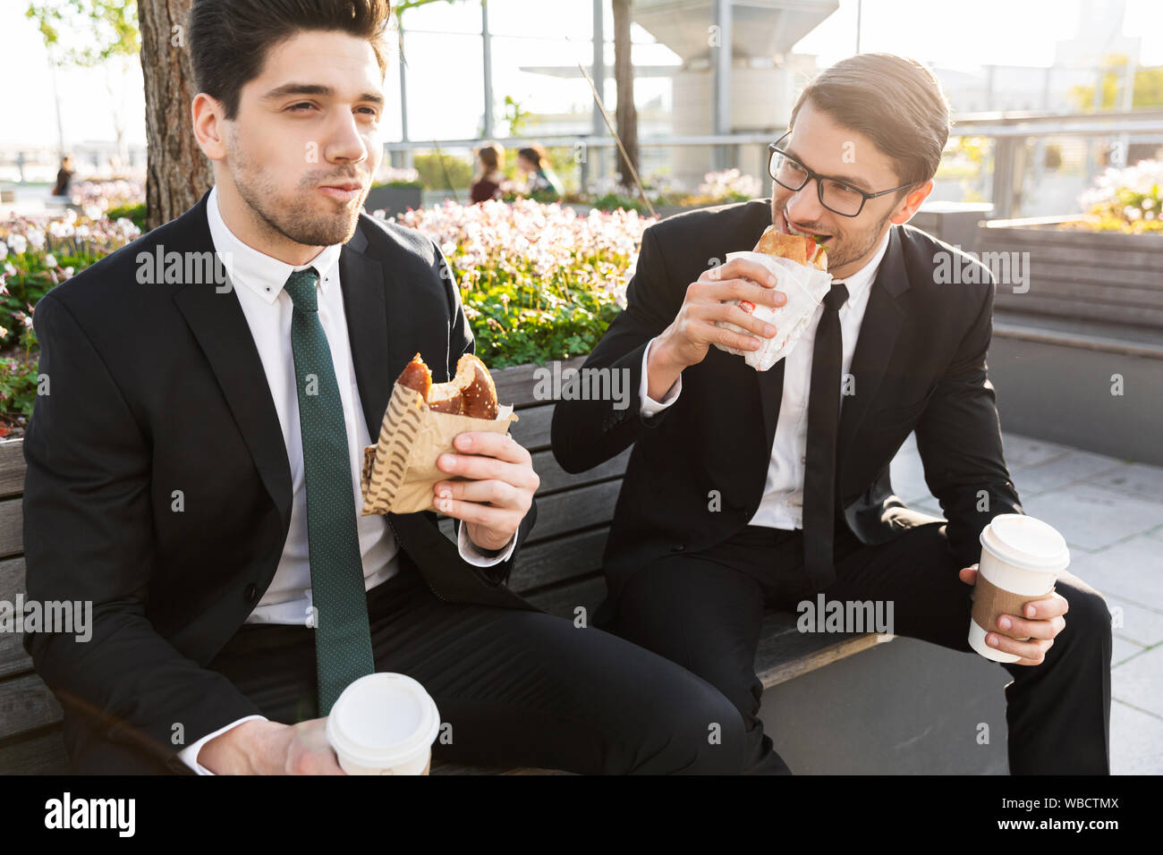 Two attractive smiling young businessmen wearing suits talking while ...