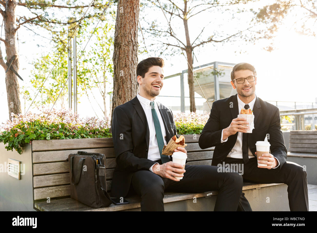Two attractive smiling young businessmen wearing suits talking while ...