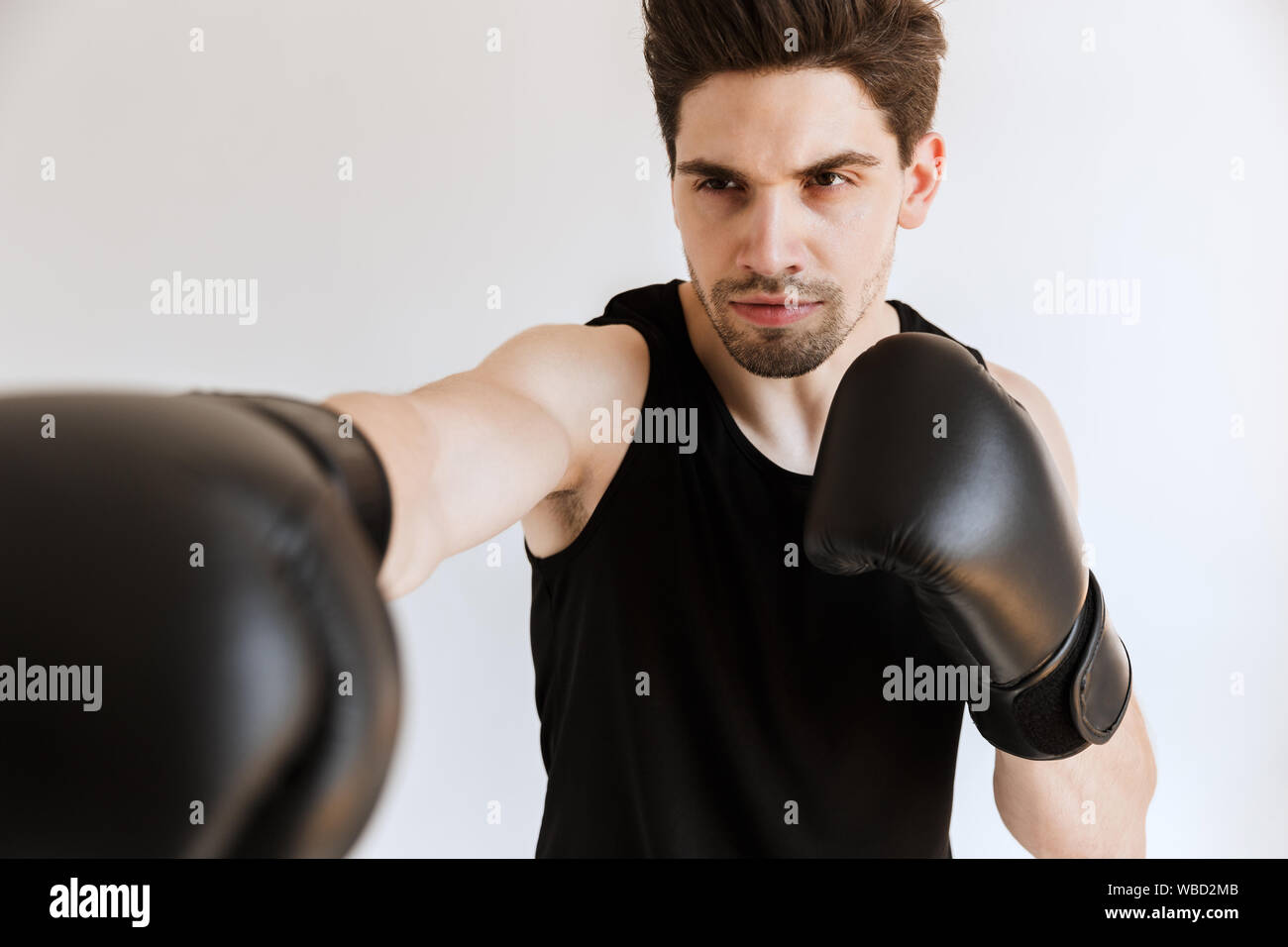 Image of a handsome strong concentrated young sports man boxer in gloves make exercises isolated