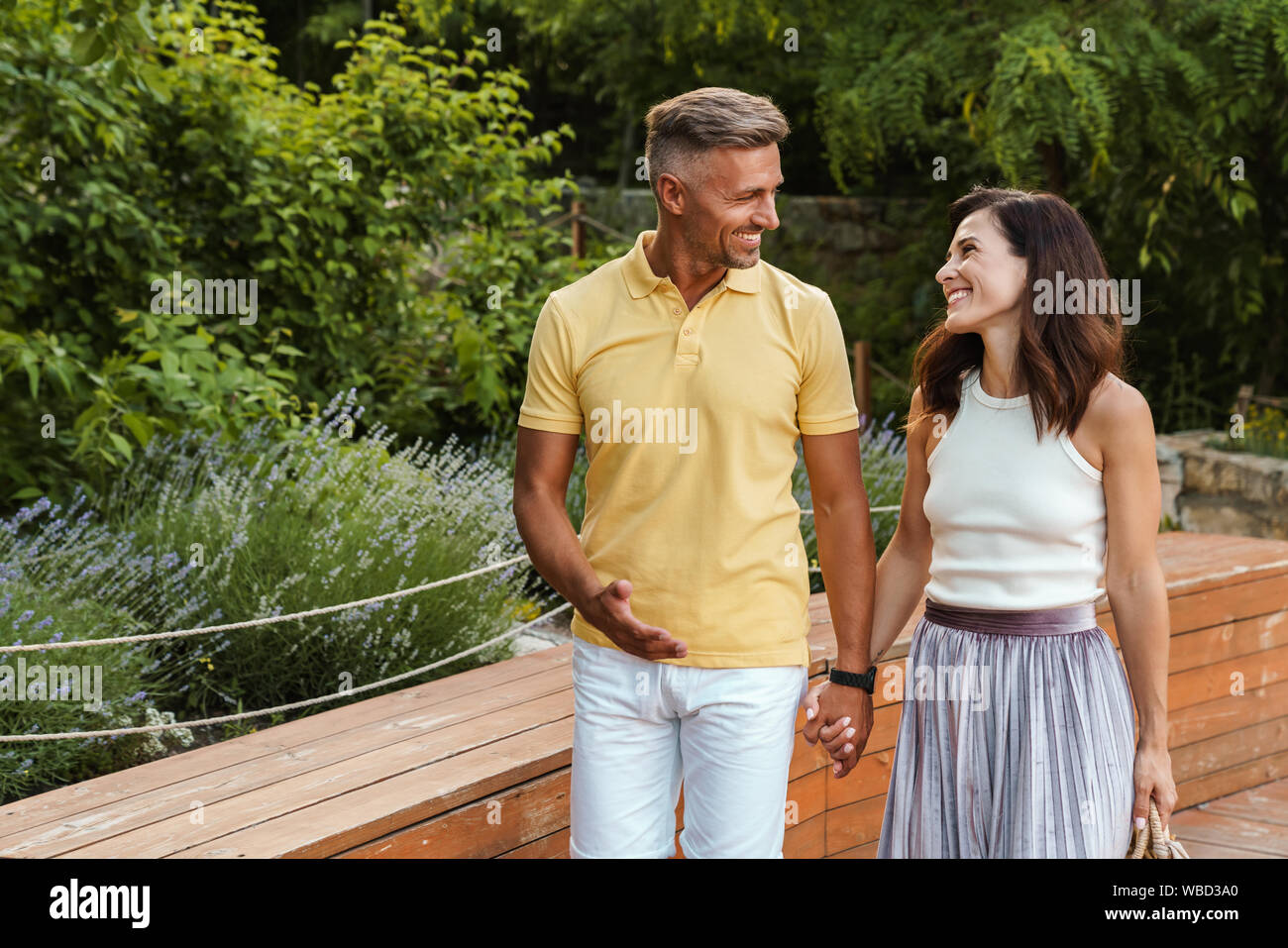 Portrait of smiling middle-aged couple man and woman holding hands together while walking in summer park Stock Photo