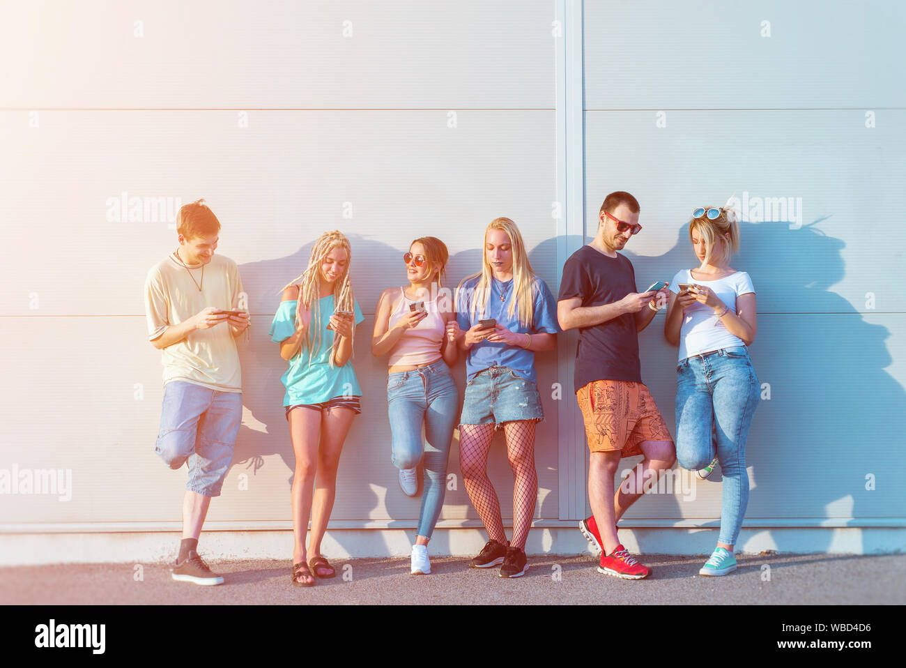 Group of young friends using their mobile phones in front of a wall Stock Photo