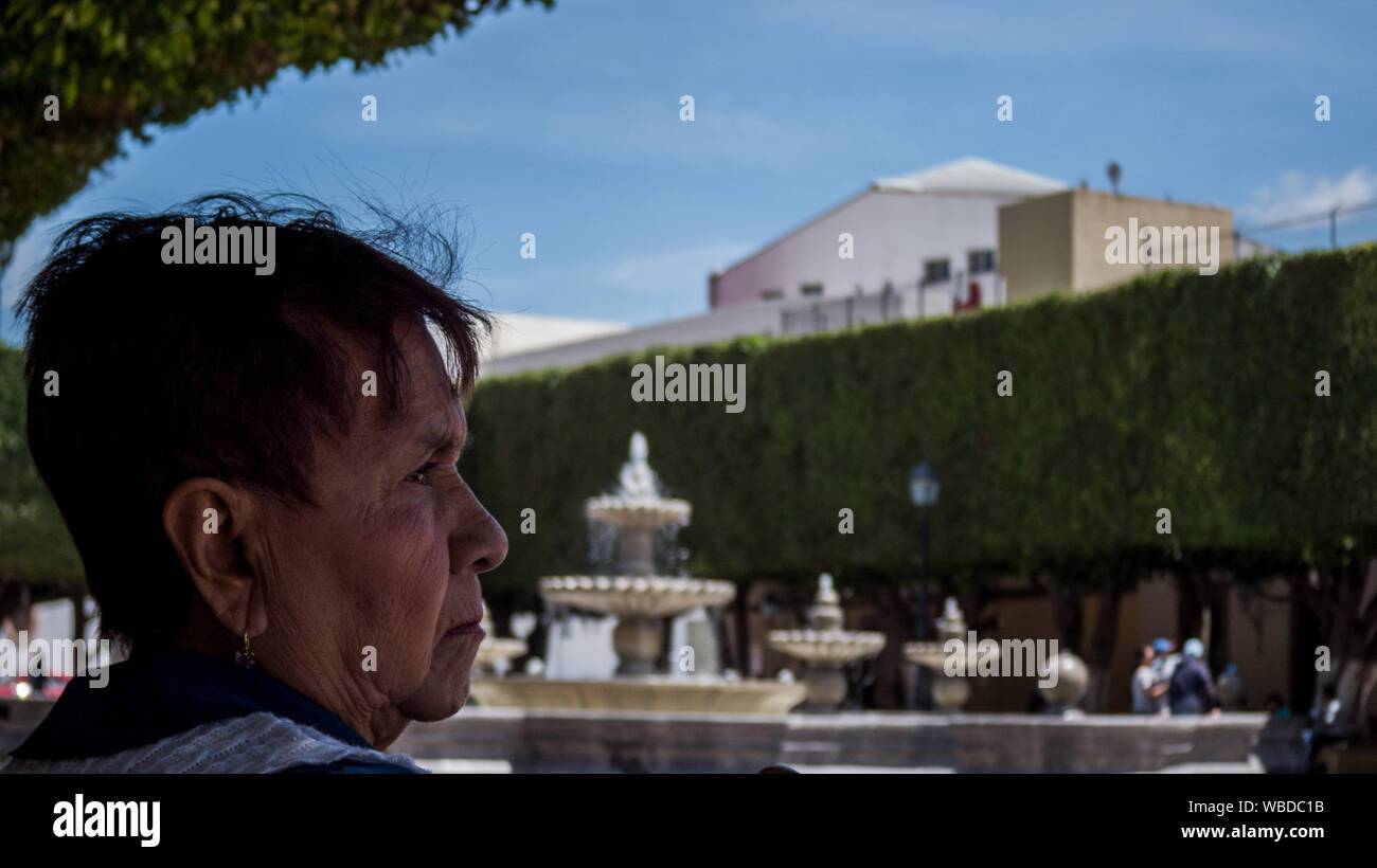 Old mexican woman sitting in the park looking away to the right Stock Photo